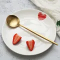 Goldener edelstahllöffel mit weißem keramikeller und frischen erdbeeren für tischdeko. - Speiselöffel / Gold