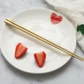Goldenes Edelstahl-Stäbchenset mit dekorativem weißem Keramikteller und frischen Erdbeeren. - Essstäbchen / Gold