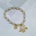 Bracelet de perles blanches de style chinois avec détails dorés et pendentif porte-bonheur. - Pendentif serrure de longévité blanche avec clochette
