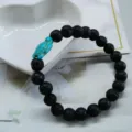 Close-up of a natural black lava stone beaded bracelet with a turquoise turtle charm on heart dish - Lava Stone - Turtle