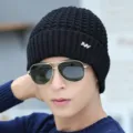 Close-up detail of mens black knitted beanie hat with metal NY logo and winter style. - Black