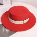 Close-up detail of red summer straw hat with chic white ribbon and metallic M logo. - One Size / Red