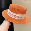 Detail view of a chic orange straw hat featuring a wide white ribbon and shiny gold letters. - Adjustable / Orange