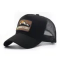 Detailed close-up of the black mesh trucker cap featuring an embroidered mountain patch. - Black