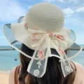 Vista dettagliata di un cappello da sole in paglia da donna con fiocco floreale ricamato. - Crema
