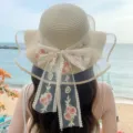 Detailed view of women beach sun hat with lace bow and floral embroidery by ocean. - Beige