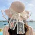 Detail view of wide brim straw sun hat with elegant lace floral bow ribbon for beach vacation. - Pink
