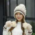 Detailed view of a woman wearing a cream knitted winter hat with matching fur gloves. - Off White