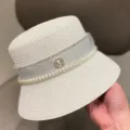 Detail view of a white straw bucket hat featuring pearl string, ribbon, and rhinestone M logo. - M (56-58cm) / White