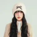 Detail view of women's autumn winter knit beanie hat with cute black bow, cozy warm pullover cap. - One Size / Off White