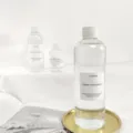 Detailed view of clear plastic home fragrance refill bottle on gold tray with decor props. - [Velvet Peony] Aromatherapy Essential Oil 300ml + 5 Reed Diffuser Sticks