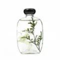 Dettaglio in primo piano di una bottiglia di vetro piatta trasparente con fiori conservati. - Gardenia bianco puro / Circa 100ml