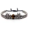Close-up detail of the micro-pave zircon crown and tiger eye stone beads on a black cord bracelet. - 2