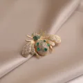 Elegant crystal bee brooch featuring sparkling rhinestones and green gems on gold tone metal. - Gold