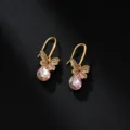Elegante goldene Schmetterlingsohrringe mit rosa Kristalltropfen auf schwarzem Leder. - Schmetterling-Anhänger / Rosa