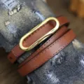 Close-up detail of a brown thin genuine leather women belt with golden oval metal buckle. - Caramel color