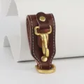 Detailed view of brown leather belt key holder with durable brass hook and neat white stitching. - Coffee