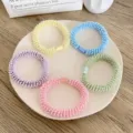 A set of five colorful pastel spiral elastic hair ties arranged on a white ceramic plate. - Fuzzy Thick Style