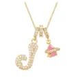 Macro detail of a gold letter J pendant necklace with a sparkling pink teardrop stone. - Letter J