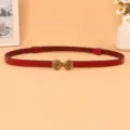 Close-up view of the red thin leather belt featuring a vintage metallic knot buckle detail. - Red