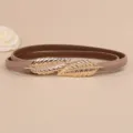 Vista dettagliata della cintura sottile in pelle da donna con fibbia a foglia d'oro elegante. - Kaki