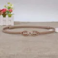 Vista dettagliata della elegante cintura sottile da donna in pelle beige con fibbia di perle. - Kaki
