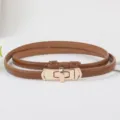 Detailed view of women's brown thin leather belt with elegant golden metal lock buckle. - Caramel color