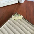 Élégante barrette à cheveux avec fleurs en tissu crème et feuilles vertes sur un plateau - Triple Fleur / Blanc Cassé