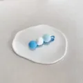 Mignonne pince à cheveux avec trois pompons en peluche bleus et blancs sur plat - Trois Bleus