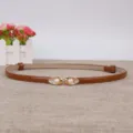 Detail van bruine smalle lederen riem met elegante gouden gesp en parelversiering. - camel