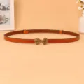 Detail shot of a brown slim leather belt with retro metal buckle for women's dress. - Camel