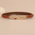 Close-up of thin brown leather belt featuring a chic double leaf golden metal buckle detail. - Camel