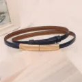 Close-up of a glossy navy blue leather thin belt with a minimalist gold buckle - Blue
