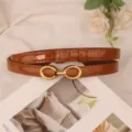 Detailed view of women thin brown patent leather belt with elegant gold double ring buckle. - Polished Camel