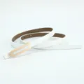 Primo piano della cintura sottile in pelle bianca minimalista con elegante fibbia in metallo dorato. - Bianco