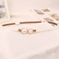 Dettaglio di un'elegante cintura sottile bianca con fibbia chic a doppia perla. - Bianco