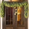 Lush artificial Norfolk pine garland with rustic brass bells on a dark wooden door - 1.8m (180 Tips With Bells)