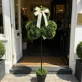 Gedetailleerd beeld van kunstmatige klaver topiary met crème strik bij een winkelingang. - Pot Stijl / Klavergroen