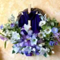 Detailed close-up of an Easter cross wreath featuring a purple drape and white lilies - 45cm / Cross Wreath (Purple Scarf)