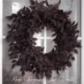 Detailed view of a moody burgundy artificial leaf wreath hanging on a white door frame - Halloween Eucalyptus Leaf Wreath