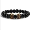 Gros plan detail de bracelet perles de pierres precieuses noires avec breloques couronne or. - Agate noire