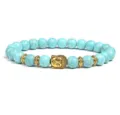Close-up detail of turquoise bead bracelet featuring golden Buddha head and metal spacers. - Blue Imitation Turquoise