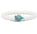 Detailed view of white beaded bracelet featuring a turquoise turtle charm centerpiece. - White