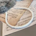 Elegant white fuzzy velvet thin headband displayed on vintage musical score paper - Flat Style / White
