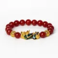 Gros plan détaillé des perles en agate rouge et du pendentif Pixiu doré sur le bracelet. - Agate rouge