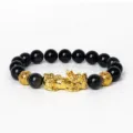 Gros plan sur le bracelet de perles noires avec un charm Pixiu doré et perles monnaie. - Obsidienne 2