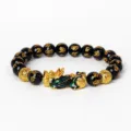 Gros plan d'un bracelet en perles d'obsidienne noire avec gravures de mantras et Pixiu doré. - Obsidienne Dorée