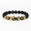 Gros plan détaillé du bracelet de perles d'obsidienne noire avec un charm Pixiu doré et bleu. - Obsidienne