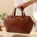 Κοντινό πλάνο καφέ φορητής τσάντας καλλυντικών με χερούλια που κρατιέται από το χέρι - Σκούρο Καφέ