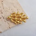 Gros plan d'une broche corail en or mat sur texture pierre, détails de design océanique. - Or